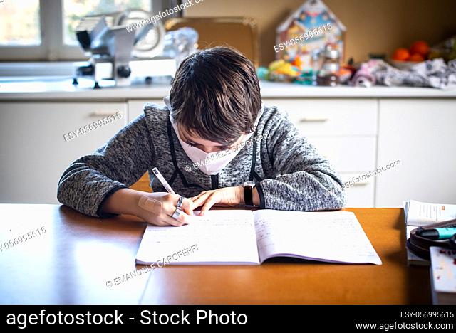 12 year old boy writes homework in notebook, mask on his face