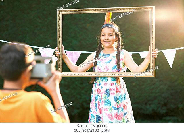 Girl looking through picture frame, having photograph taken