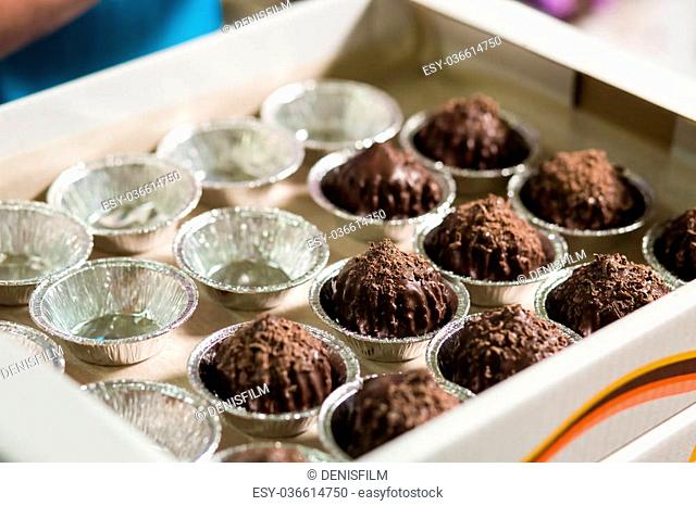 Brown sweets in small cups. Dark candies in white box. Time to pack the goods. Marketable condition of fresh dessert