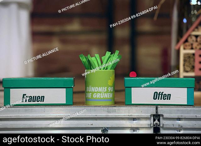 04 March 2023, Thuringia, Walldorf: Two note boxes labeled ""Women"" and ""Open"" and a cup with green pens stand on the stage at the state delegates'...
