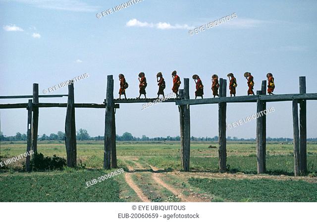 Line of monks crossing two hundred and fifty year old bridge over flood plain near Mandalay