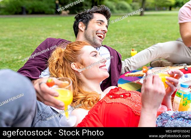 Happy friends with drink resting during picnic at park
