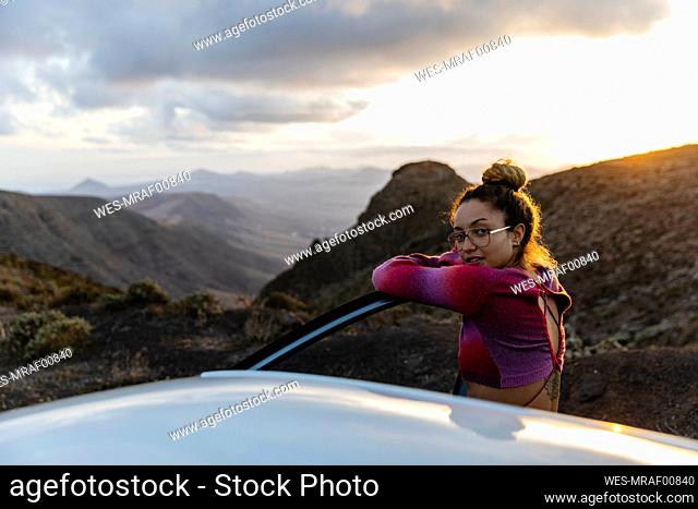 Woman leaning on car door with mountains in background