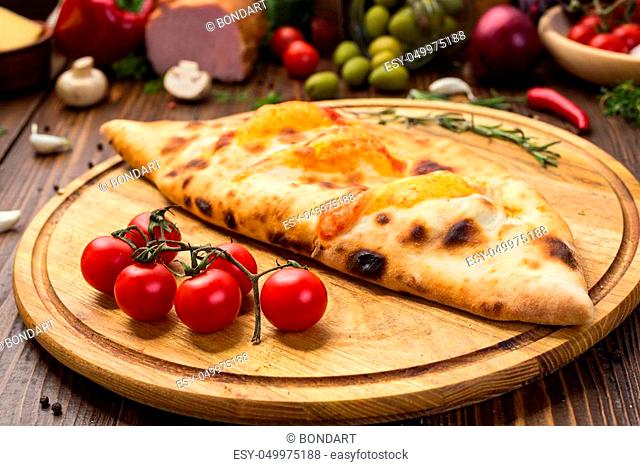 Traditional italian closed pizza Calzone with basil leaves on wooden background