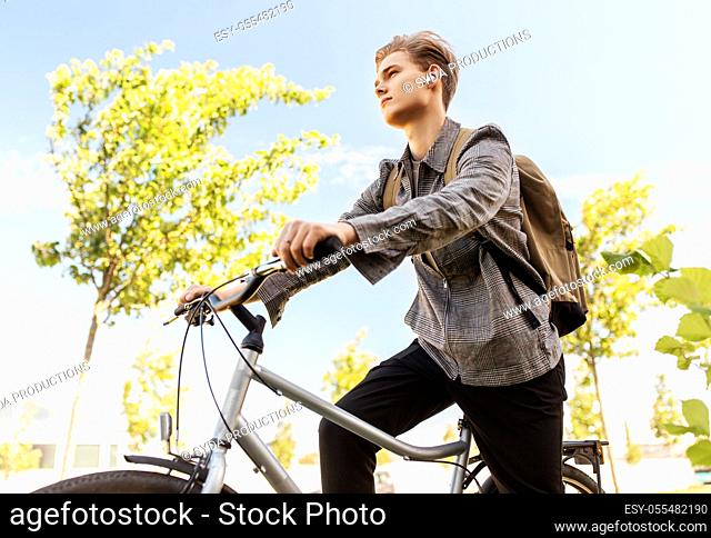 teenage boy with earphones and bag riding bicycle