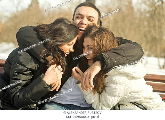Three young adults hugging on park bench in winter