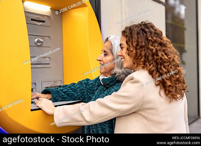 Happy senior woman with granddaughter buying ticket through machine