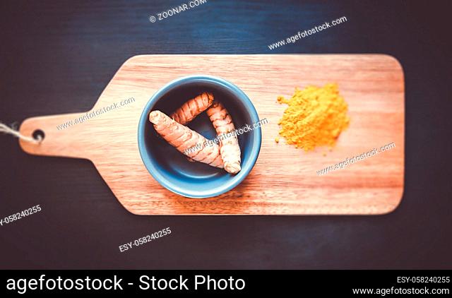 Turmeric root in bowl and spice powder on a wooden cutting board. Top view