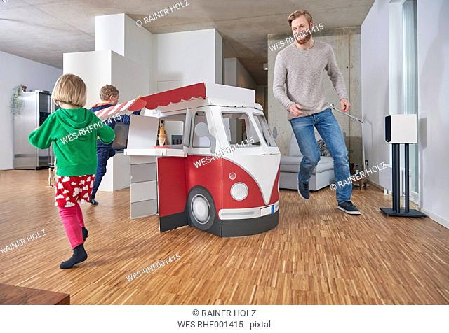 Happy father with children running around model car in living room