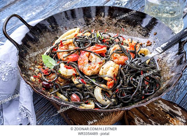 Italian linguine con tinta de calamari and prawns with olives as close-up in a wroth iron pan