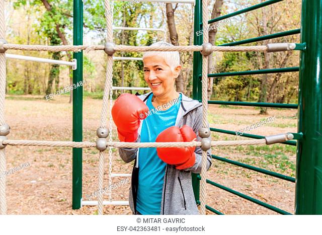 Portrait Of Happy Fit Senior Woman With Boxing Glove At Outdoor Gym In Sportswear. Active Old People Fitness Lifestyle