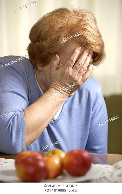 A senior woman sitting at a table covering her face with her hand