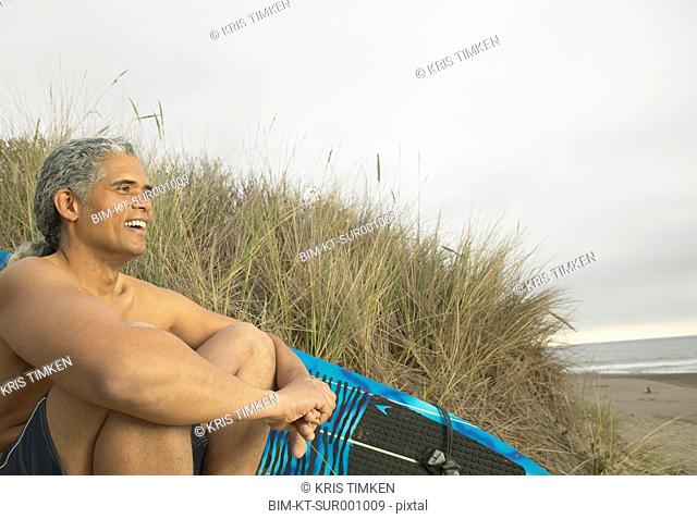 Senior man sitting on the dunes with a surfboard Oakland, California, United States