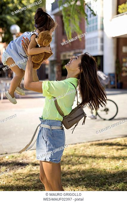 Happy mother lifting up daughter outdoors in the city