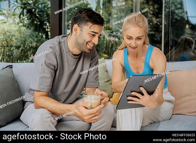 Woman sharing smart phone with man holding coffee cup at lounge