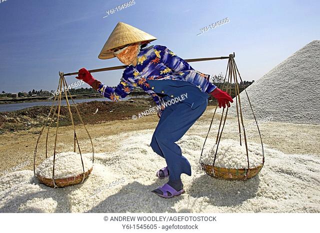Woman in conical hat prepares to dump pannier baskets of salt on a new salt mound Vietnam