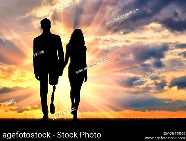 Concept of support and assistance to people with disabilities. Disabled person with a prosthetic leg, walking with a woman holding hands at sunset