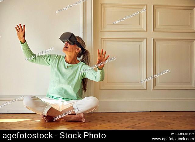 Woman using VR glasses while sitting on hardwood floor at home