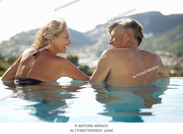 Mature couple relaxing together in pool, rear view