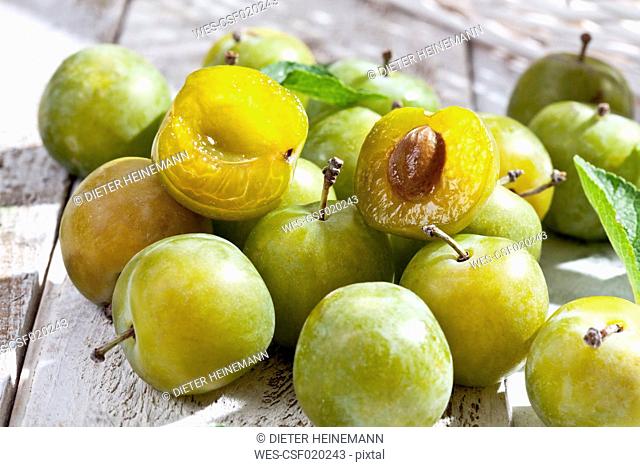 Sliced and whole greengages (Prunus domestica subsp. italica var. claudiana) on white wooden table, studio shot