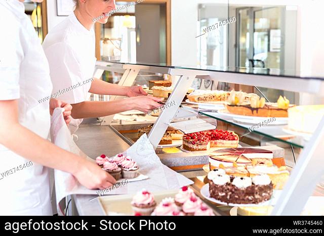 Women in pastry shop filling up sales display with pies and cakes