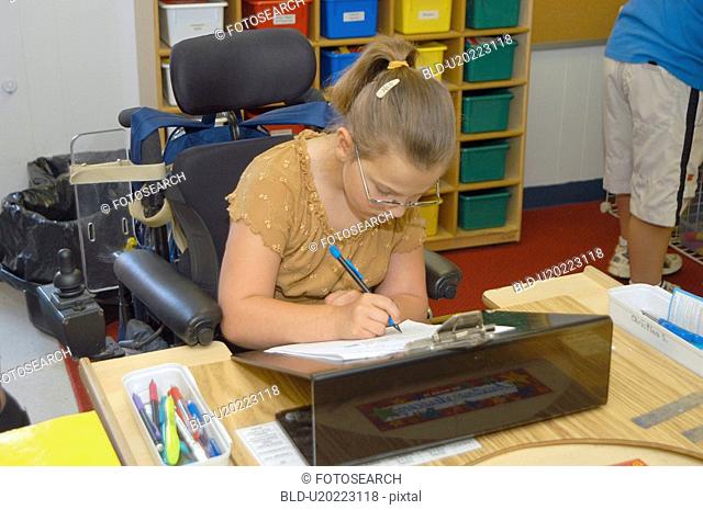 Girl, with multiple physical disabilities, doing her school work in class. She utilizes a power wheelchair for mobility