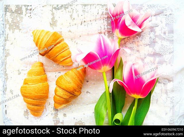 Three croissants and bright pink tulips on lace tablecloth, close-up