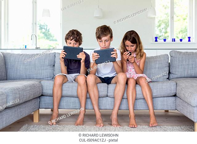 Brothers and sister on sofa with digital tablets and mobile