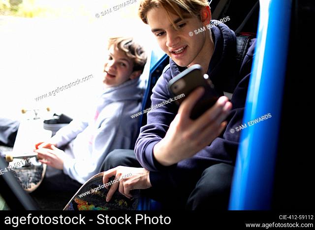 Teenage boys with smart phone and skateboards at car