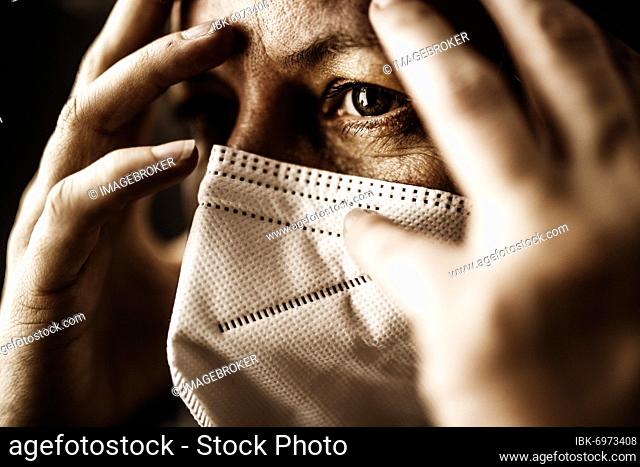 Woman with FFP2 medical mask looks thoughtful and holds hands to her head, studio shot, Germany, Europe