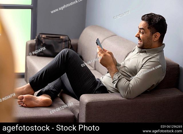 Young businessman using mobile phone while leaning on sofa at home