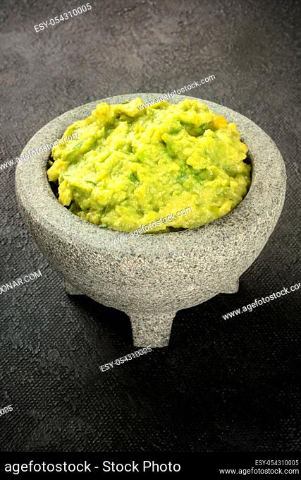 Guacamole in a molcajete, Mexican avocado dip sauce in the traditional stone mortar, on a black background with a place for text