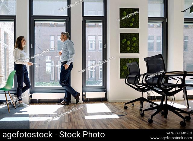 Man and woman talking while leaning on wall at office