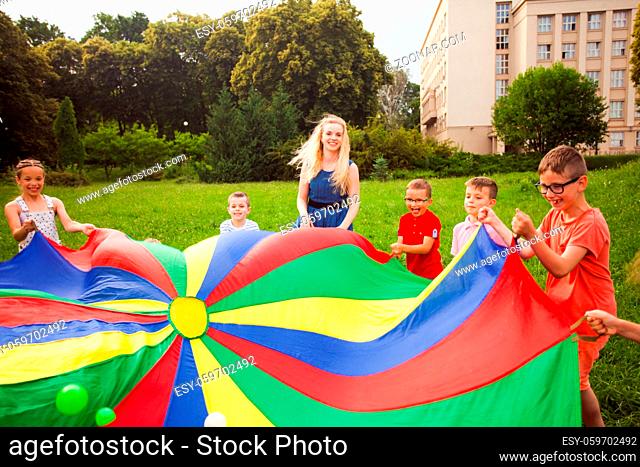Happy friends enjoying with rainbow parachute full of balls outdoors