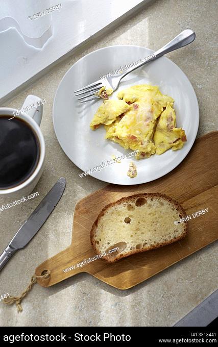A kitchen counter with scrambled eggs, toast, coffee, and streaks of sunlight