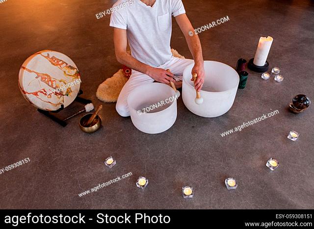 Man sitting in indian with his two big crystal bowls and his native sacred drum, playing sacred music in a meditative state. Shot from above