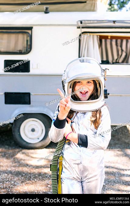 Girl wearing space suit showing peace sign while standing against motor home