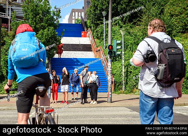 11 August 2021, Hamburg: Hamburgers and tourists walk up and down the St. David's Stairs in the St. Pauli district, painted in the HSV colors of blue