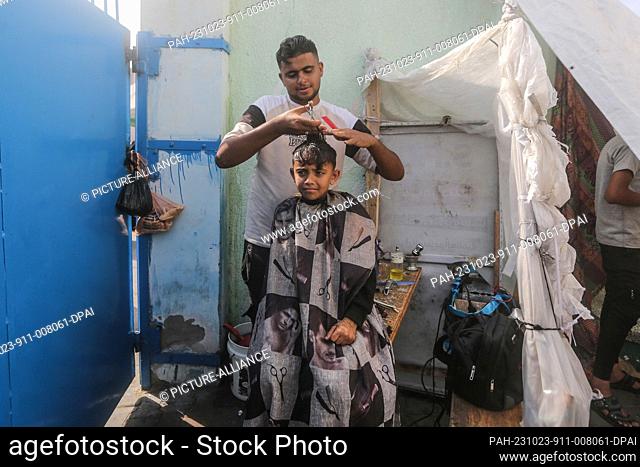23 October 2023, Palestinian Territories, Khan Yunis: A volunteer barber gives a haircut to a palestinian child at a UN-run school