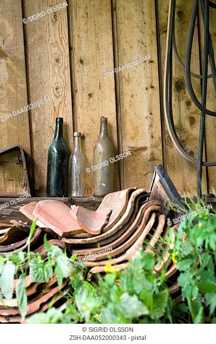 Old glass bottles, broken clay tiles stacked by wall outdoors