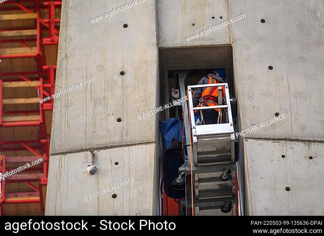 03 May 2022, Saxony-Anhalt, Magdeburg: Workers stand in a basket hanging between a pylon of the future bridge at the construction site ""replacement new power...
