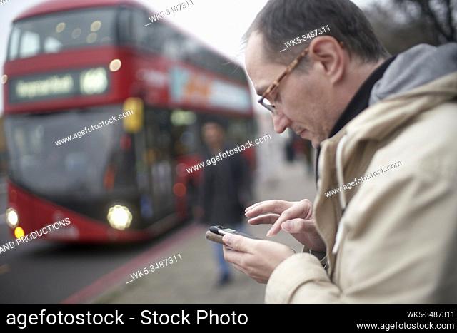 man using smartphone app at bus station in South London, UK