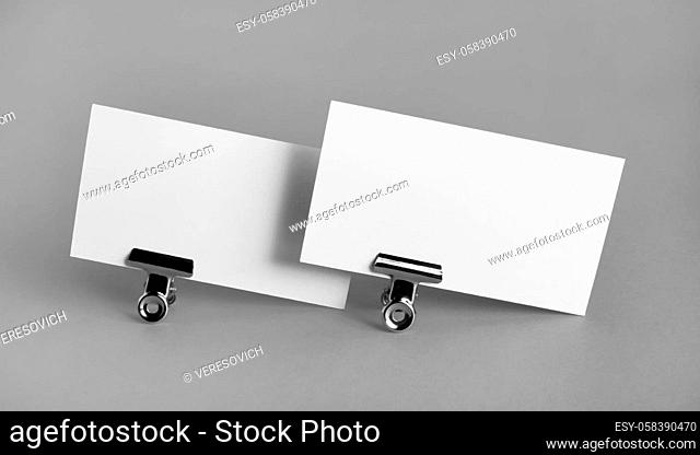 Two blank business cards and metal binder clips on gray background. Mockup for branding identity