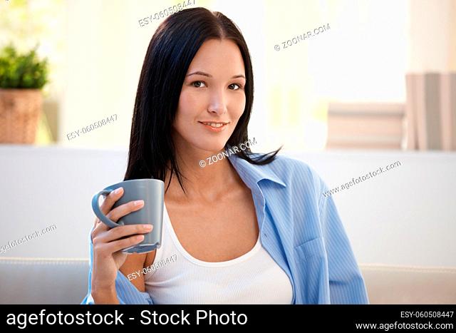 Portrait of young smiling woman holding coffee cup, looking at camera