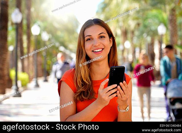 Young hispanic girl smiling happy using smartphone at the esplanade of Alicante, Spain