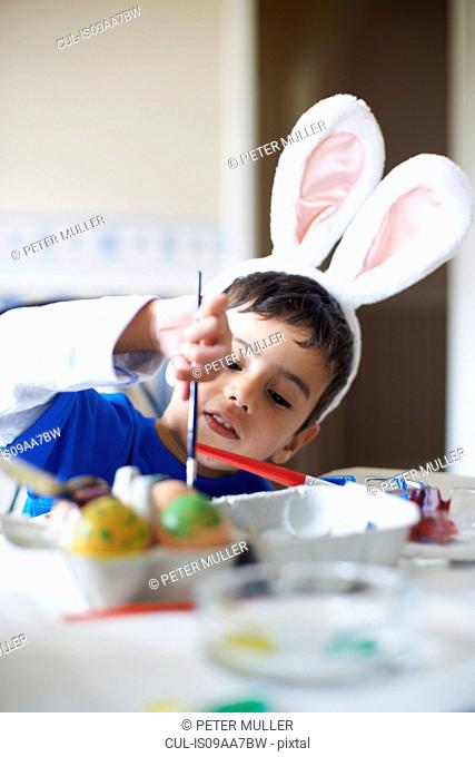 Boy wearing bunny ears painting Easter eggs