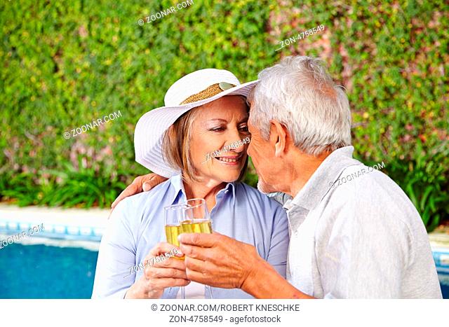 Zwei glückliche Senioren sitzen mit einem Glas Sekt am Pool eines Hotels
