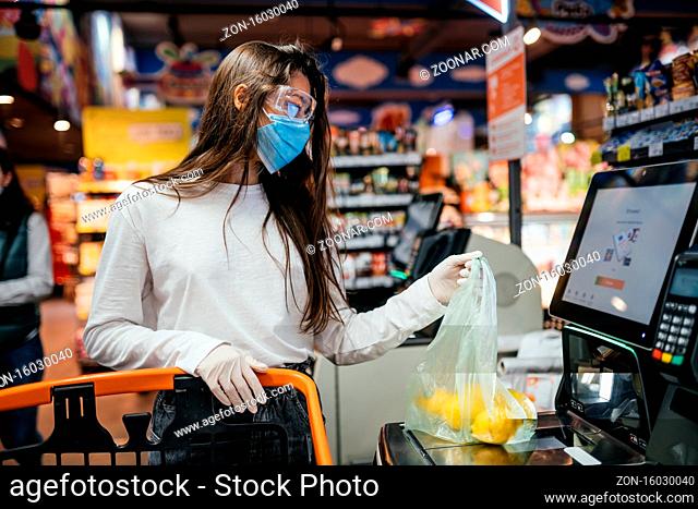 A young woman scans products in a mask and gloves. Self-checkout counter in the food store during coronavirus epidemic