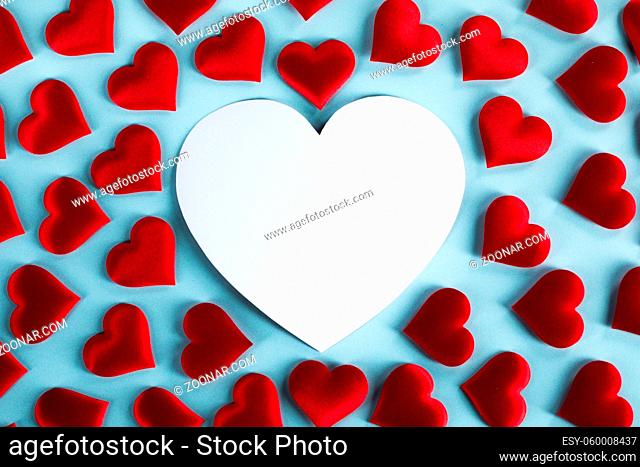 Valentine's day many red silk hearts and white heart shaped card on blue background, love concept