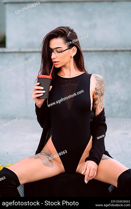 An attractive girl with a tattoo in a sexy position is drinking street coffee
